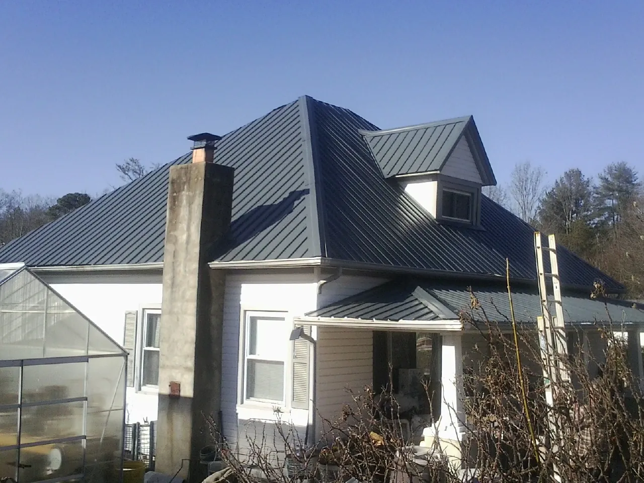 Dark blue standing seam metal roof on a white farmhouse with dormer — Slate & Tile Roof Repair by Roofing Brothers in Lovelady