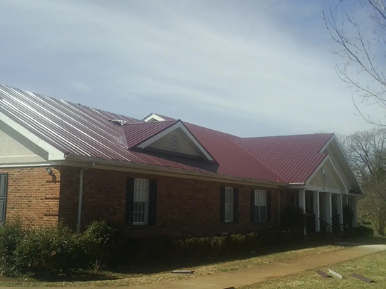 Red metal roof with gabled entries on a long brick building, from a Hail Damage Roof Repair job in Lovelady
