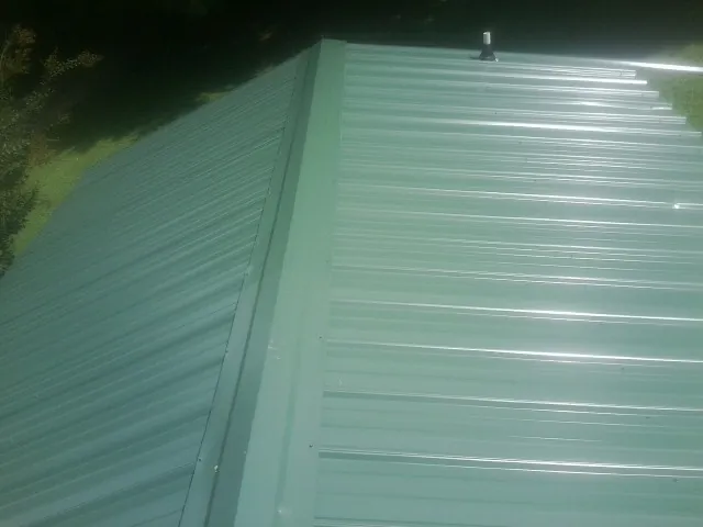 New green metal panels meeting at the ridge of a roof — Flat Roof Repair work by our crew in Lovelady