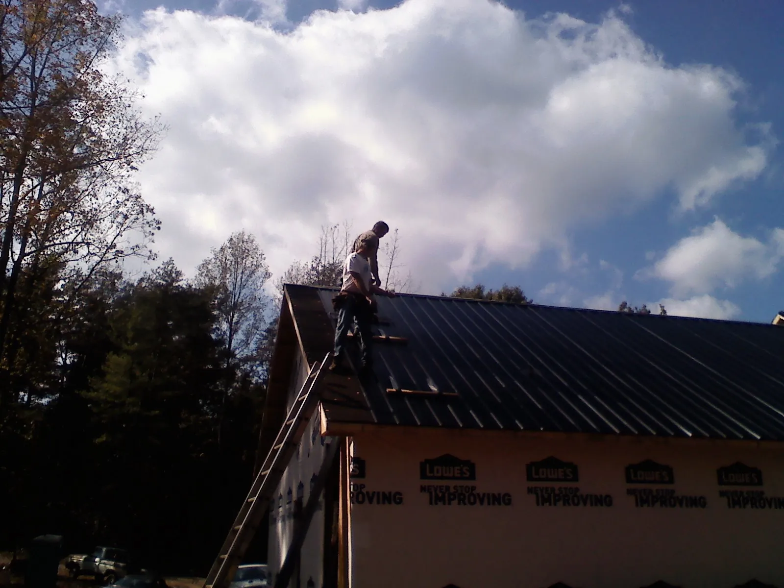 Roofer fastening dark metal panels high against a cloudy sky, from a Roof Inspection job in Lovelady