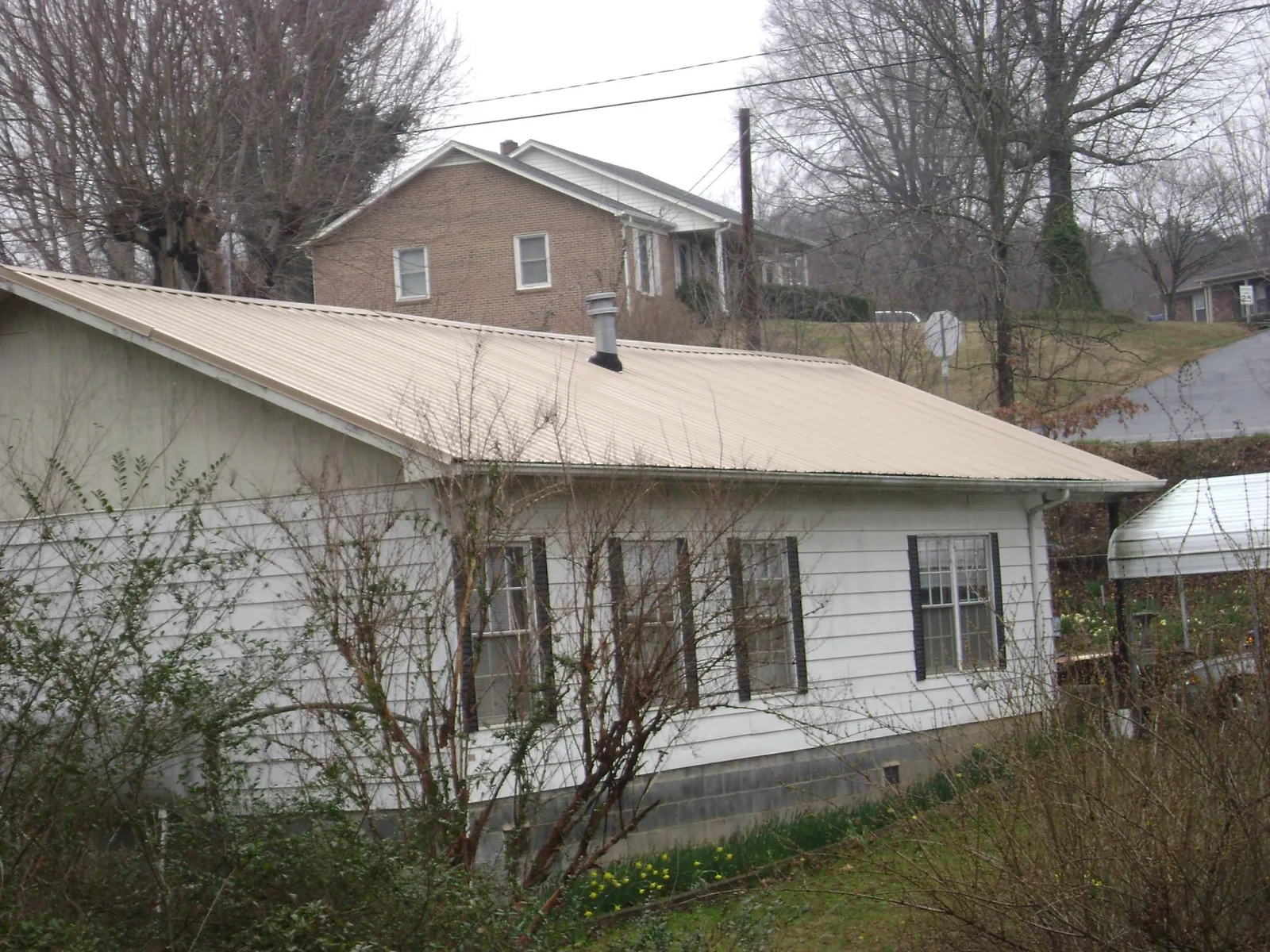 Tan metal roof on a white sided house set into a hillside — Commercial Roofing by Roofing Brothers in Lovelady