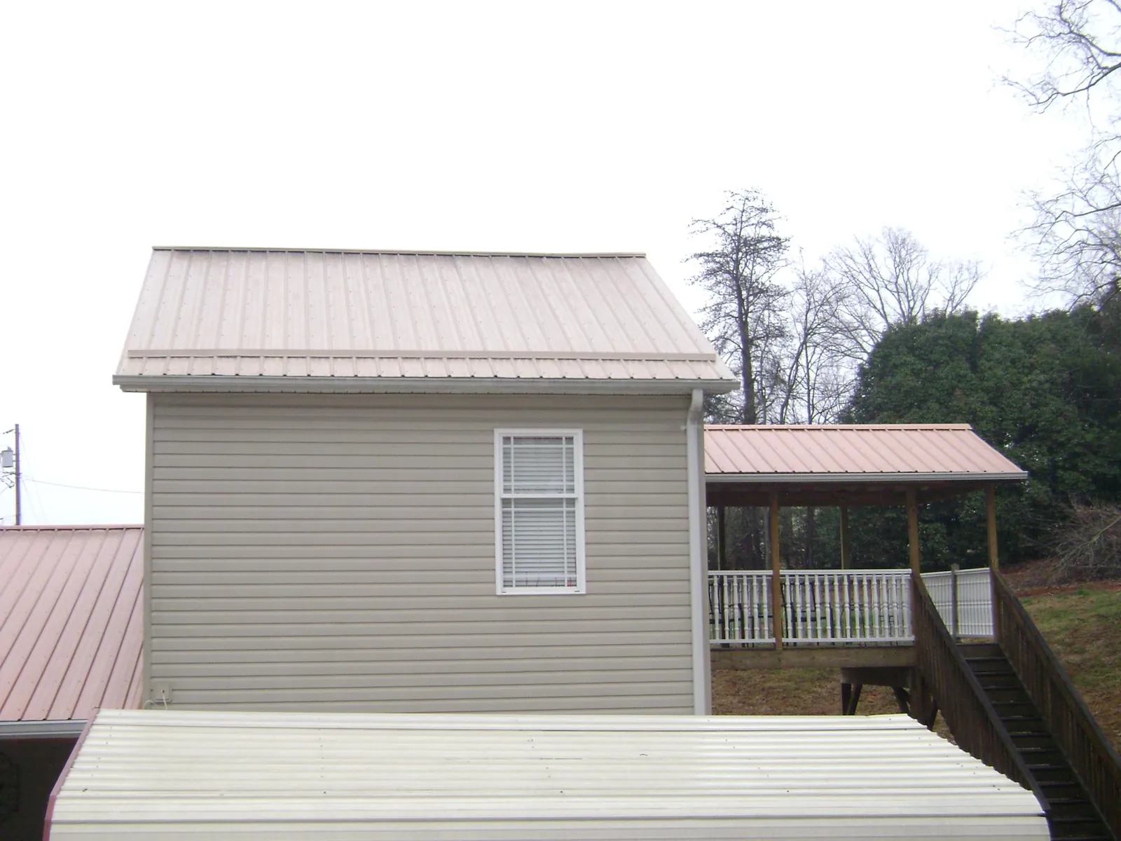 Tan metal roofs on a two story addition and attached porch, from a Roof Replacement job in Lovelady